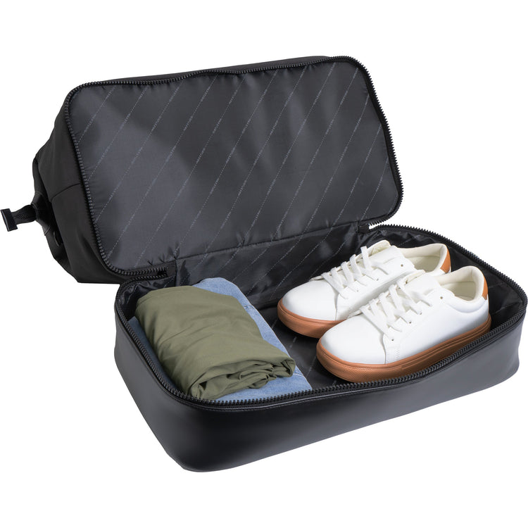 Black travel shoe bag with white sneakers and a folded green shirt inside on a white background
