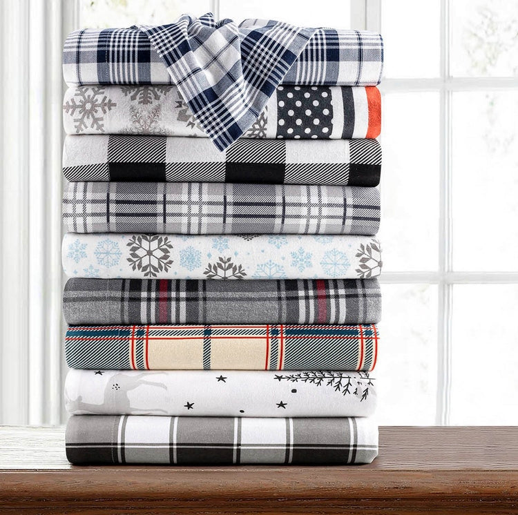 Stack of plaid and patterned blankets on a wooden surface with a window in the background.