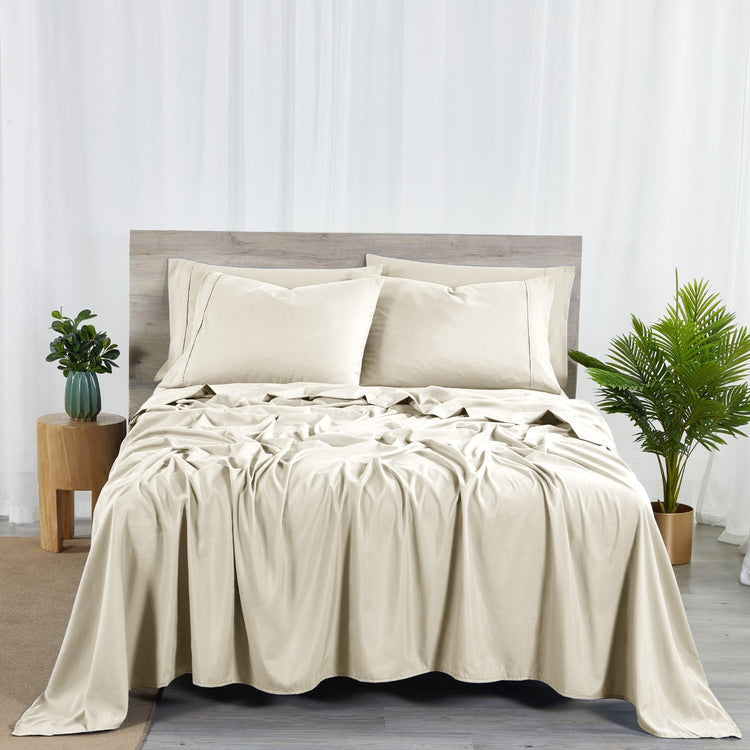 A cream-colored bamboo sheet set on a bed, including a fitted sheet, flat sheet, and pillowcases, with a wooden headboard and houseplants in the room.