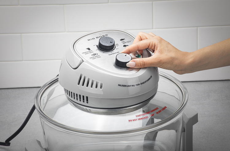 Hand adjusting controls on a white kitchen appliance with a clear lid against a tiled wall background.