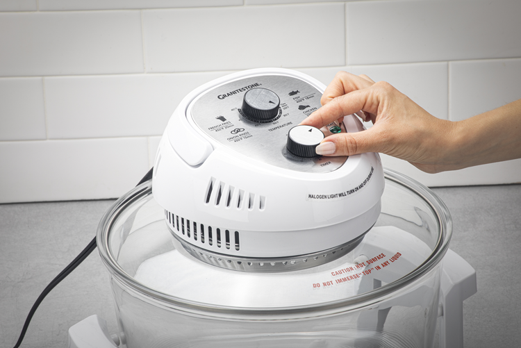 Hand adjusting controls on a white kitchen appliance with a tiled wall background