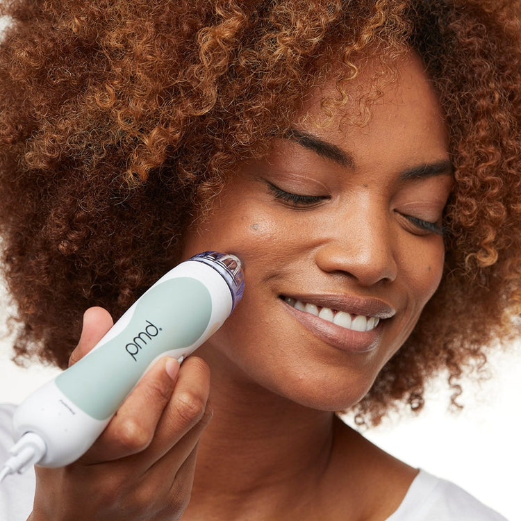 Woman using a pmd device on her face with a neutral background