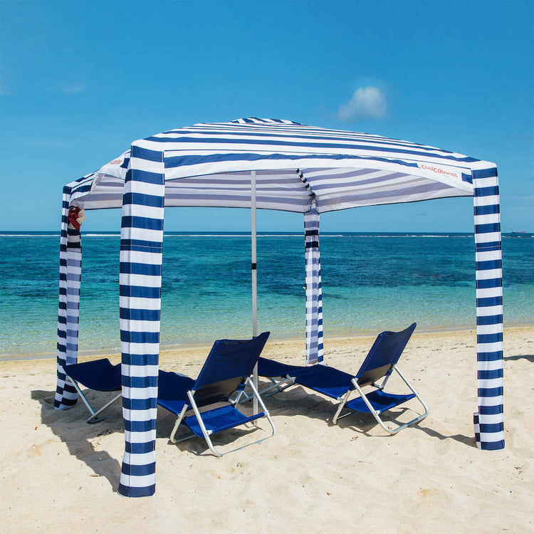 Blue and white striped beach canopy with lounge chairs on a sandy beach.