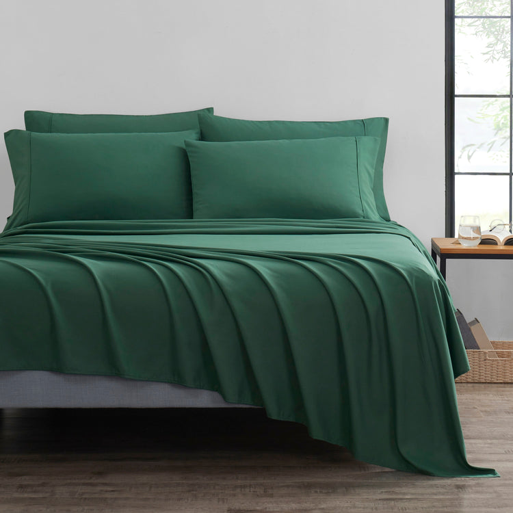 Green bed sheets and pillows on a bed in a room with a window.