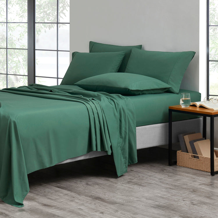 Green bedspread set on a bed in a room with large windows.