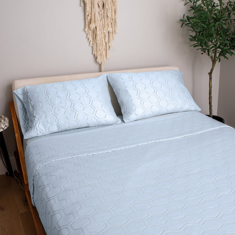 Light blue textured bedspread and pillowcases on a wooden bed in a bedroom setting.