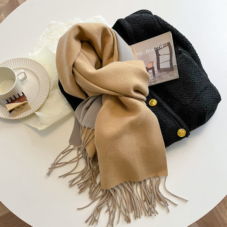 A green reversible pashmina scarf with fringe detailing, displayed on a white surface next to a beige coat and a pretzel.