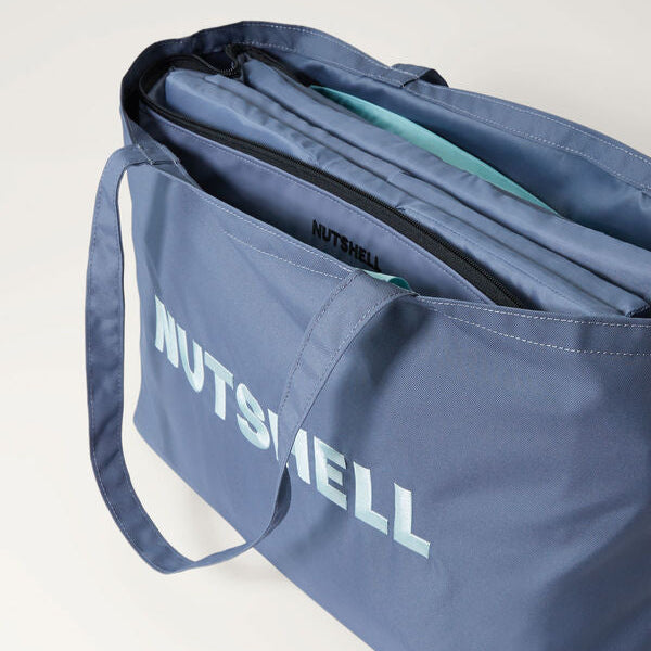 Blue tote bag with 'NUTSHELL' embroidery and folded cooler inside on a light gray background