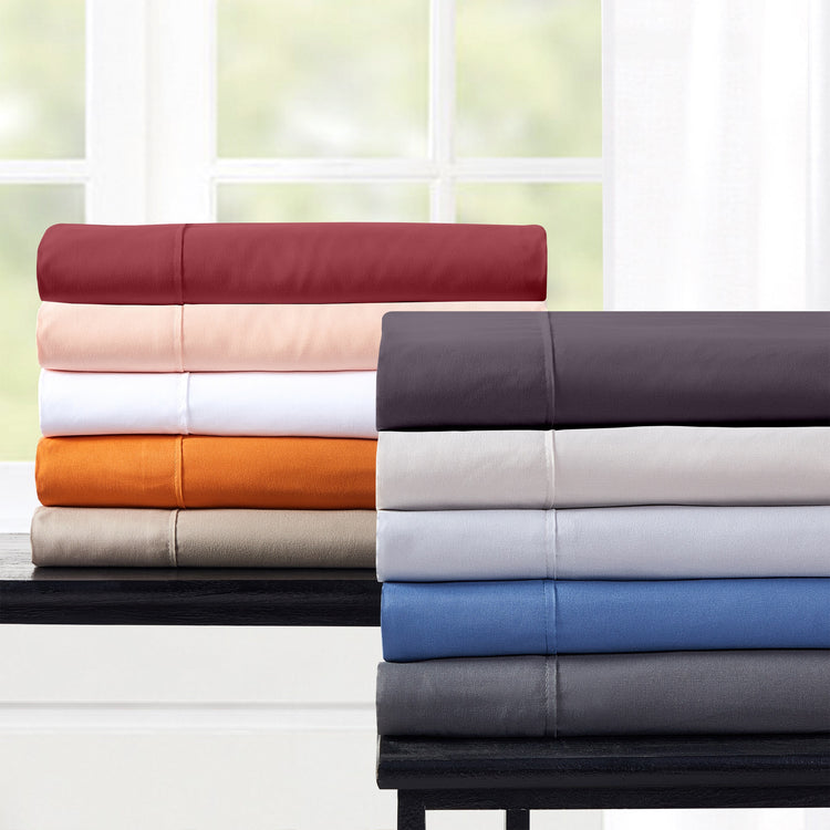 Stack of folded bed sheets in various colors on a table with a window in the background.