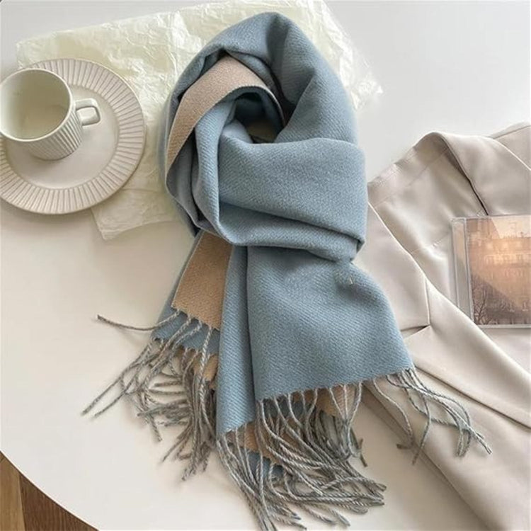 A green reversible pashmina scarf with fringe detailing, displayed on a white surface next to a beige coat and a pretzel.