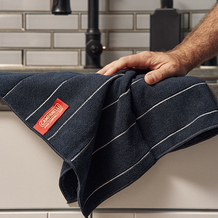 Person holding a dark blue towel with a red Campanelli label in a kitchen setting.