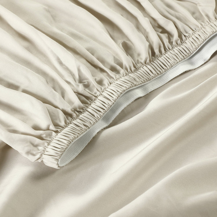 Beige fitted sheet on a bed with a close-up view of the fabric and elastic band.