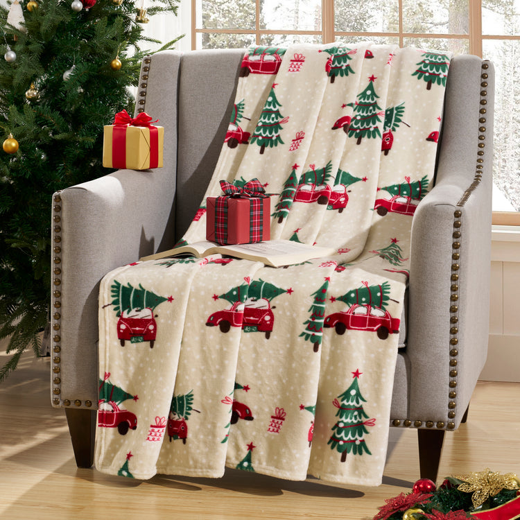 Christmas-themed blanket with red trucks and green trees draped over a chair next to a decorated Christmas tree.