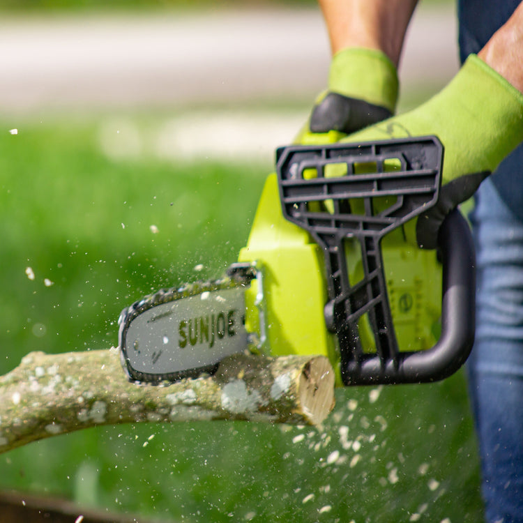 Person using a Sun Joe chainsaw to cut a branch with a blurred green background