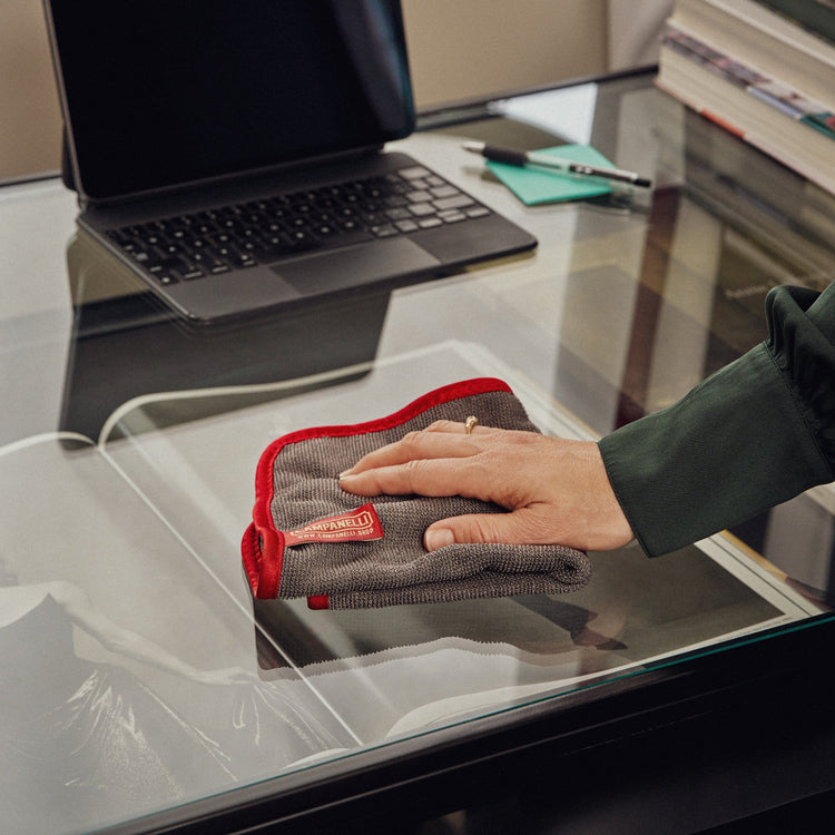 Person cleaning a glass surface with a cloth on a desk.