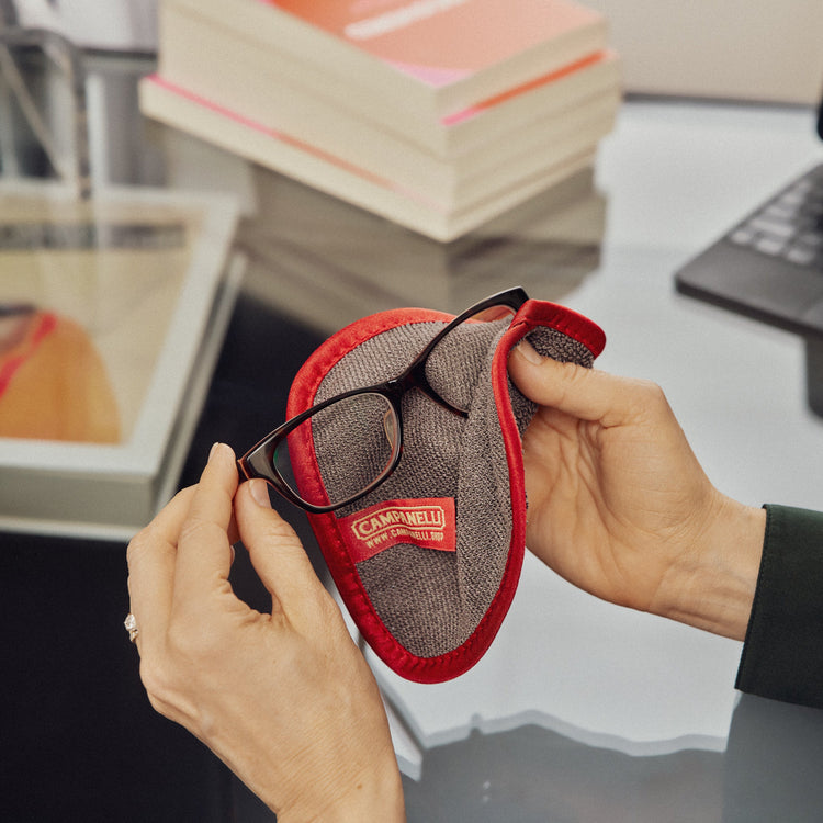 Person holding a red and gray eyeglass case with a laptop and books in the background
