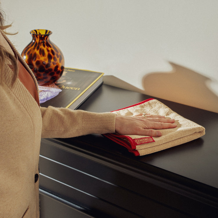 Person cleaning a surface with a cloth, with a vase and book in the background.
