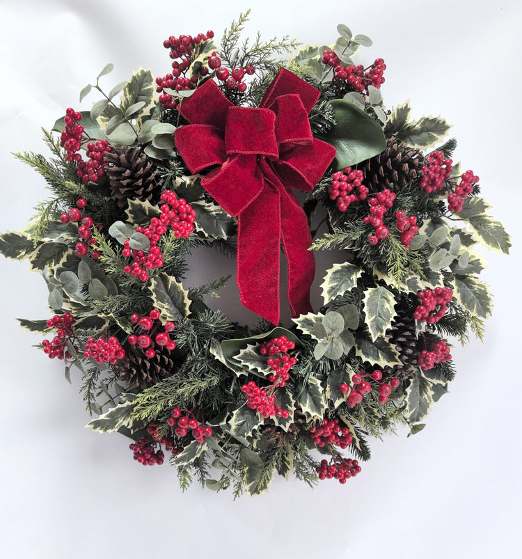 Christmas wreath with red berries, pine cones, and a red bow on a white background