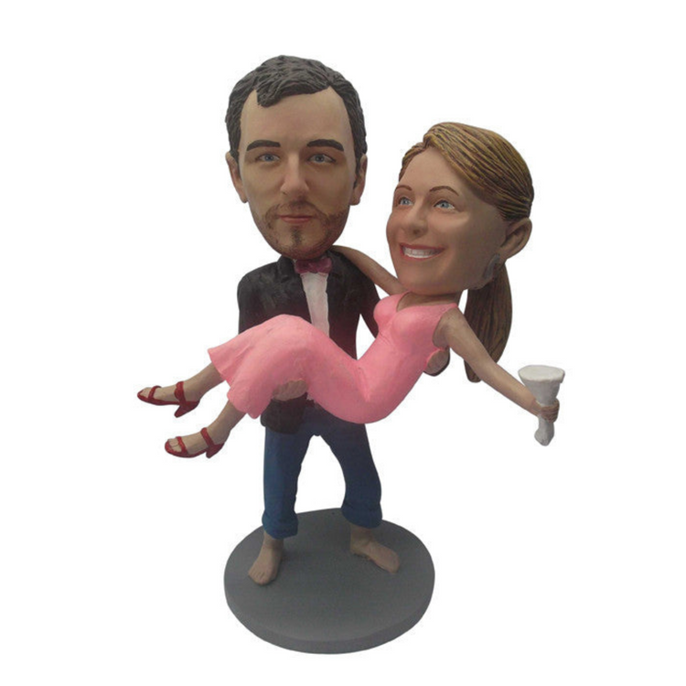 Bobblehead figurine of a man lifting a woman in a pink dress on a white background