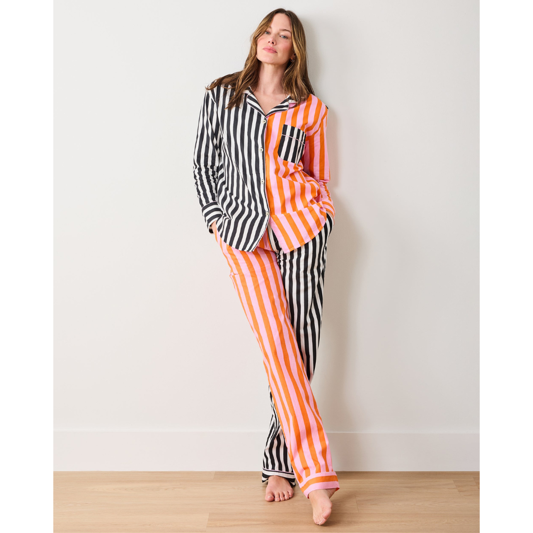 Woman wearing a black and white striped shirt with orange and white striped pants against a white wall.