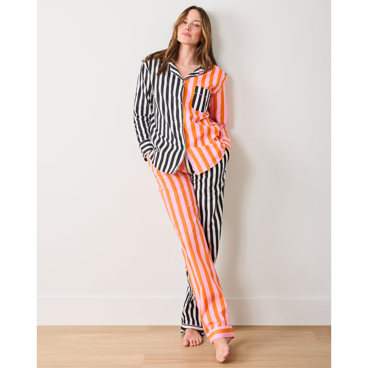 Woman wearing a black and white striped shirt with orange and white striped pants against a white wall.