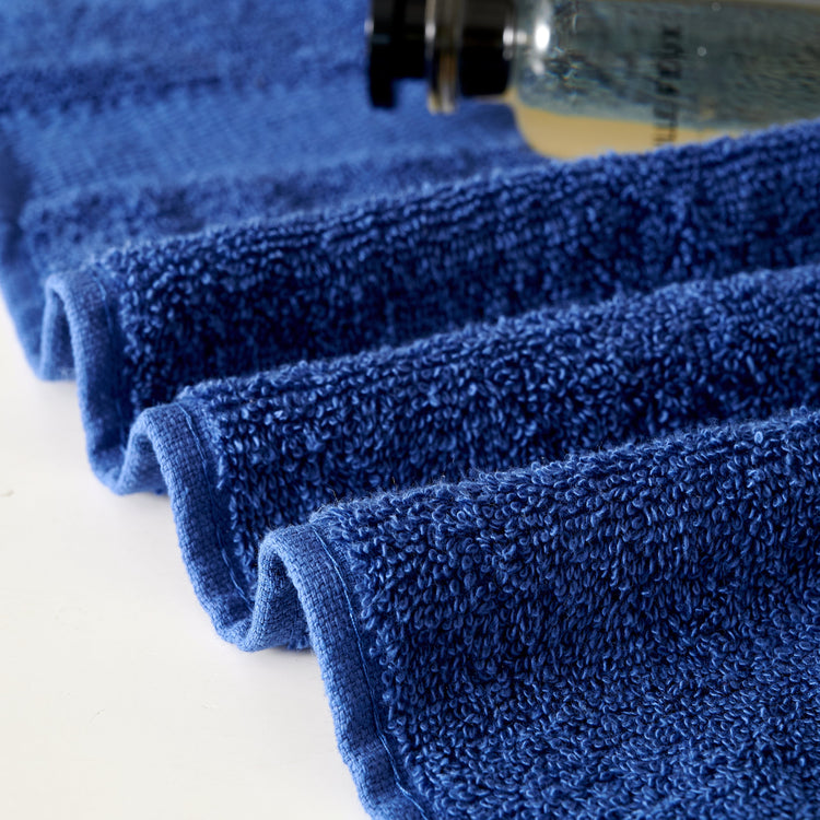 Stack of blue towels with a bottle of cleaning solution on a white background