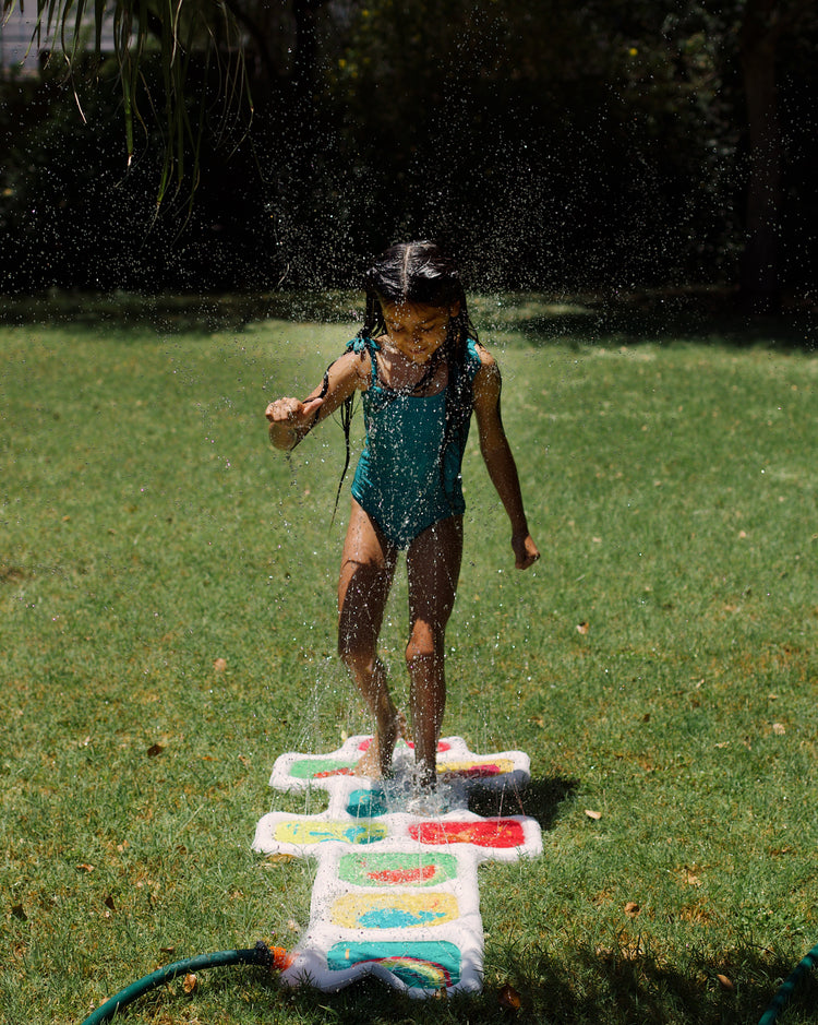 Child playing with a water sprinkler on a grassy area