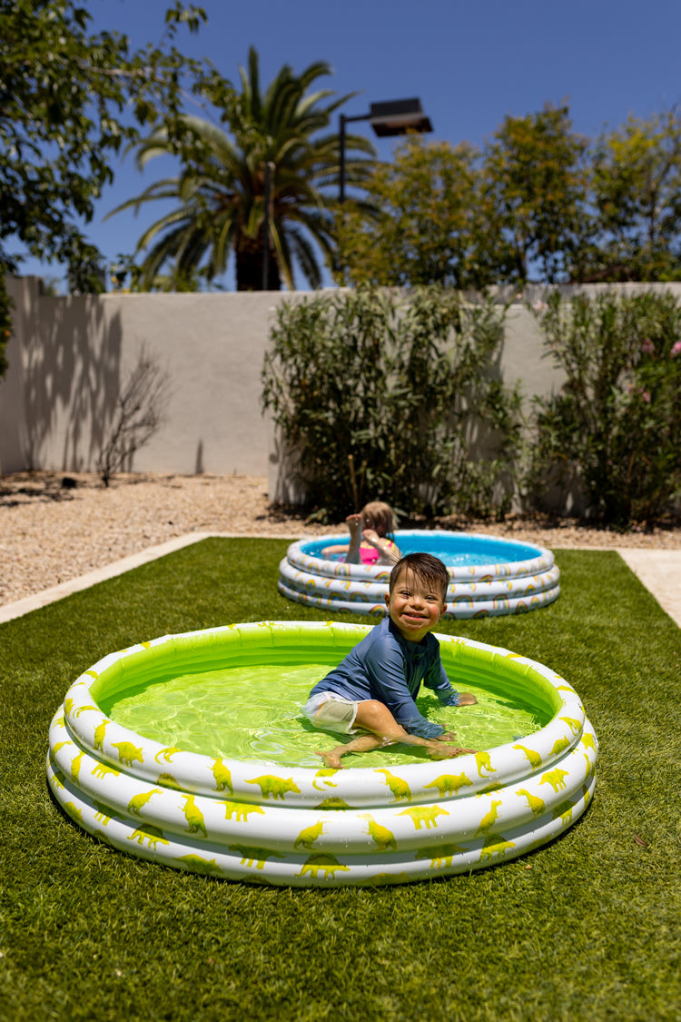 Children playing in inflatable pools in a backyard with trees and a clear sky.