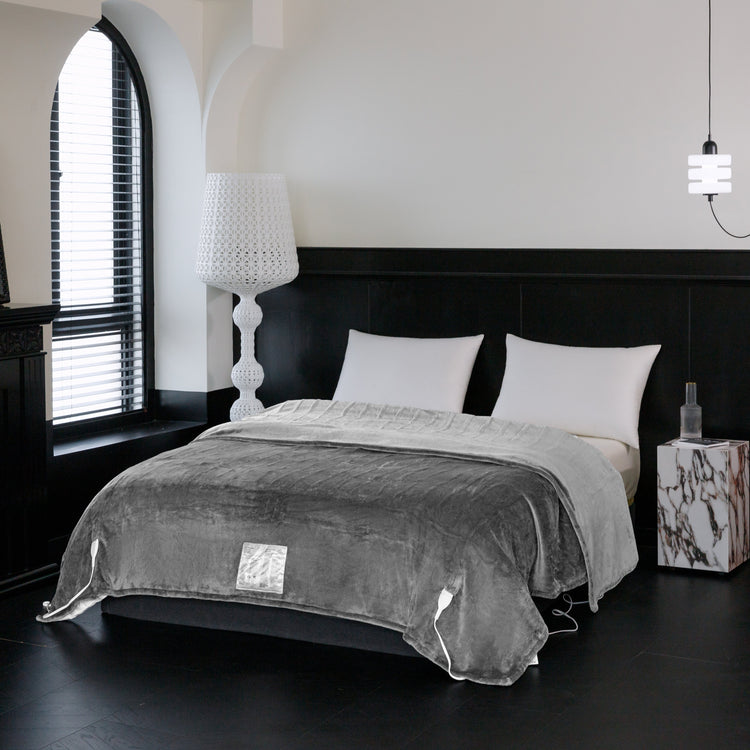 Gray blanket draped over a bed in a modern bedroom with a lamp and nightstand.