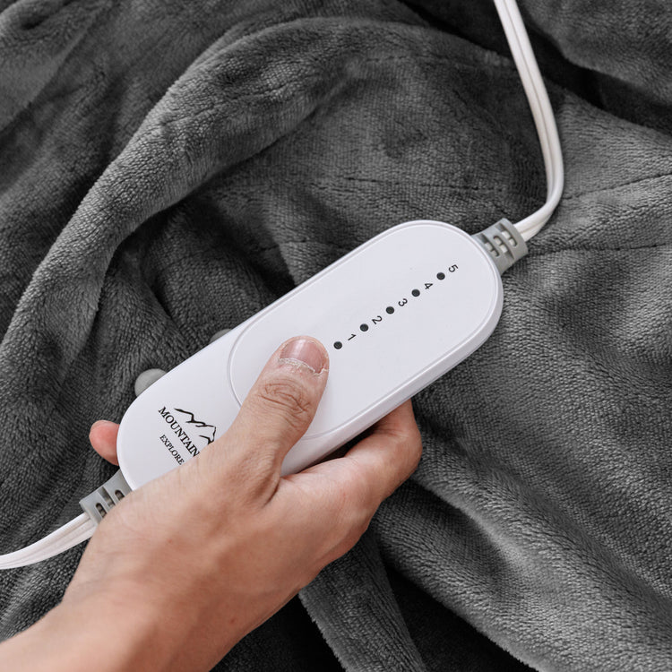 Hand holding a white electronic device with a brand logo on a gray blanket