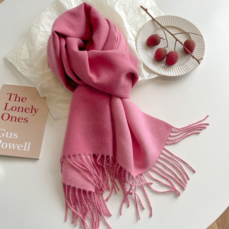 A green reversible pashmina scarf with fringe detailing, displayed on a white surface next to a beige coat and a pretzel.