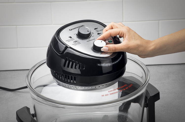 Hand adjusting a knob on a countertop appliance with a glass lid.