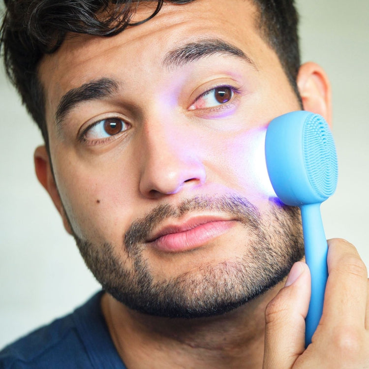 Man using a blue facial cleansing brush on his face