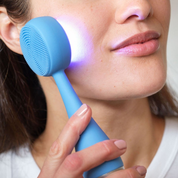 Person using a blue facial cleansing brush on their face with a close-up view.