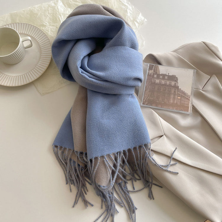 A green reversible pashmina scarf with fringe detailing, displayed on a white surface next to a beige coat and a pretzel.