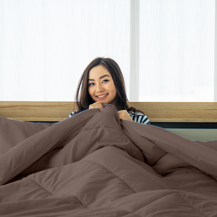 Woman peeking out from under a brown comforter in a bedroom.