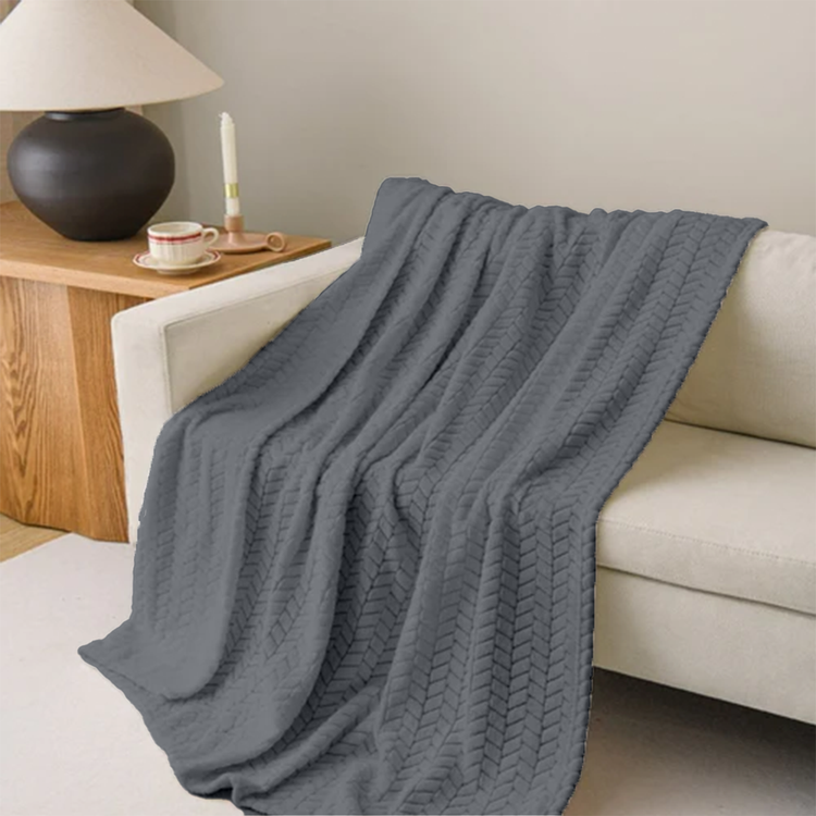 Gray knitted blanket draped over a white sofa in a living room setting.