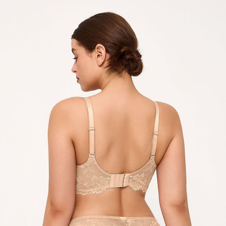 A woman shown from the back wearing a light pink lace bralette with adjustable straps and a bow detail at the center back, against a plain light background.