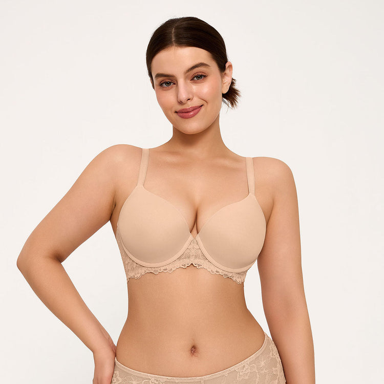 A woman modeling a light beige underwire bra with scalloped lace trim, shown against a plain light background.