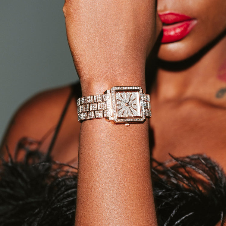 A close-up lifestyle shot of a woman wearing a square diamond-encrusted watch with a matching diamond-strap on her wrist, with her hand near her face and red lipstick visible.