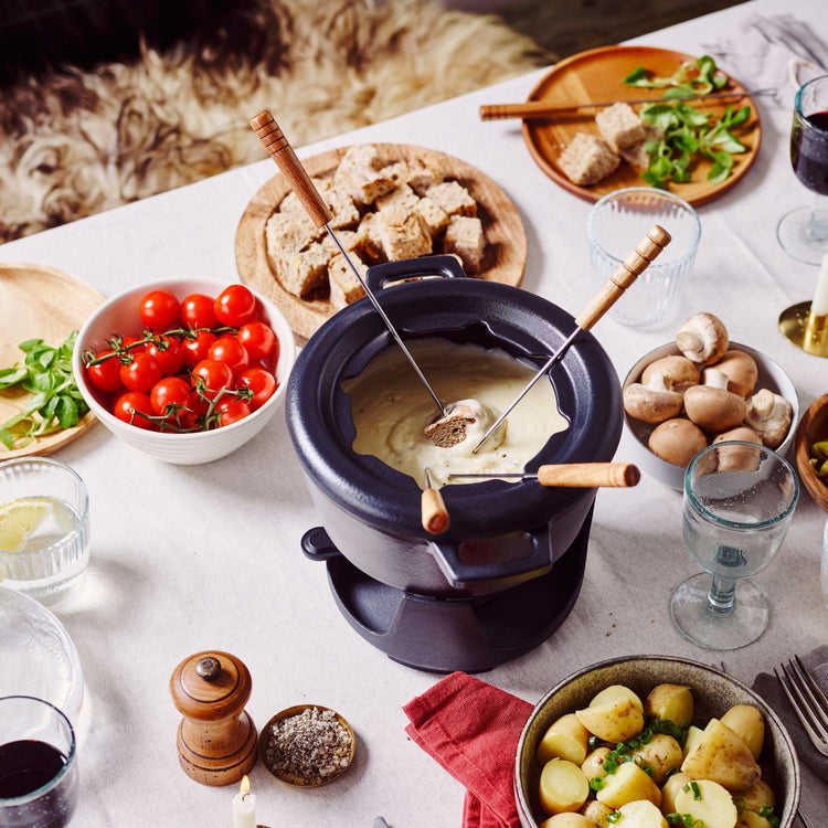 Fondue setup with bread, vegetables, and wine glasses on a table.