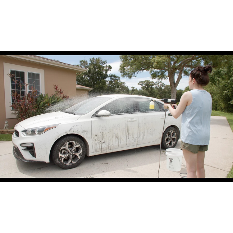 Woman washing a white car with a hose on a driveway.
