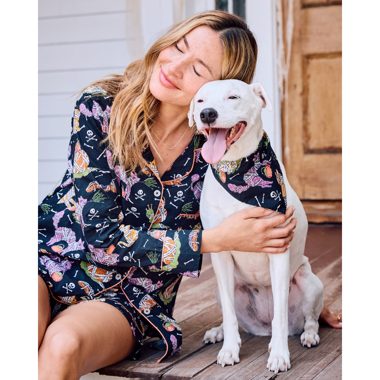 Woman in a floral robe holding a white dog on a wooden deck.