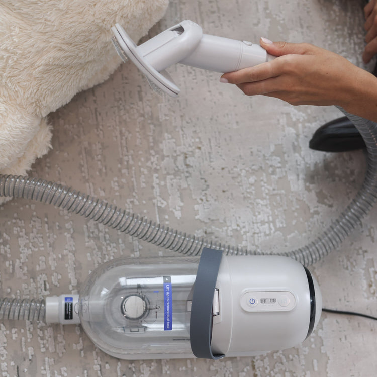 Person using a handheld vacuum cleaner on a carpeted floor.