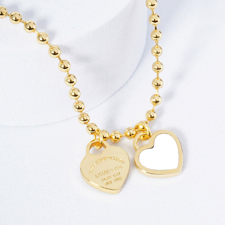 A gold-colored necklace featuring a ball chain design with two heart-shaped pendants.