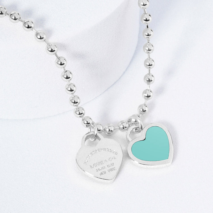 A silver necklace featuring two heart-shaped charms on a ball chain.