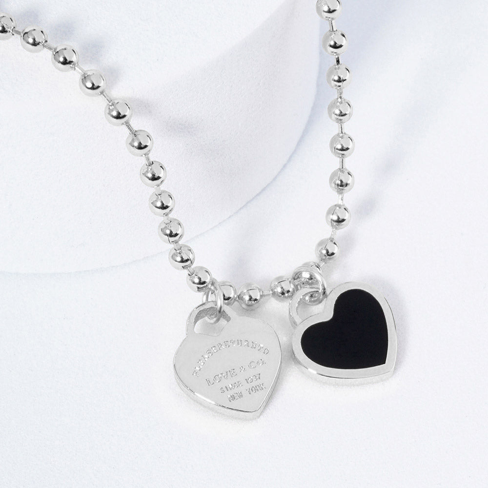 A silver necklace featuring two heart-shaped charms on a ball chain.
