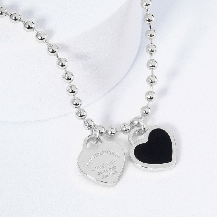 A silver necklace featuring two heart-shaped charms on a ball chain.
