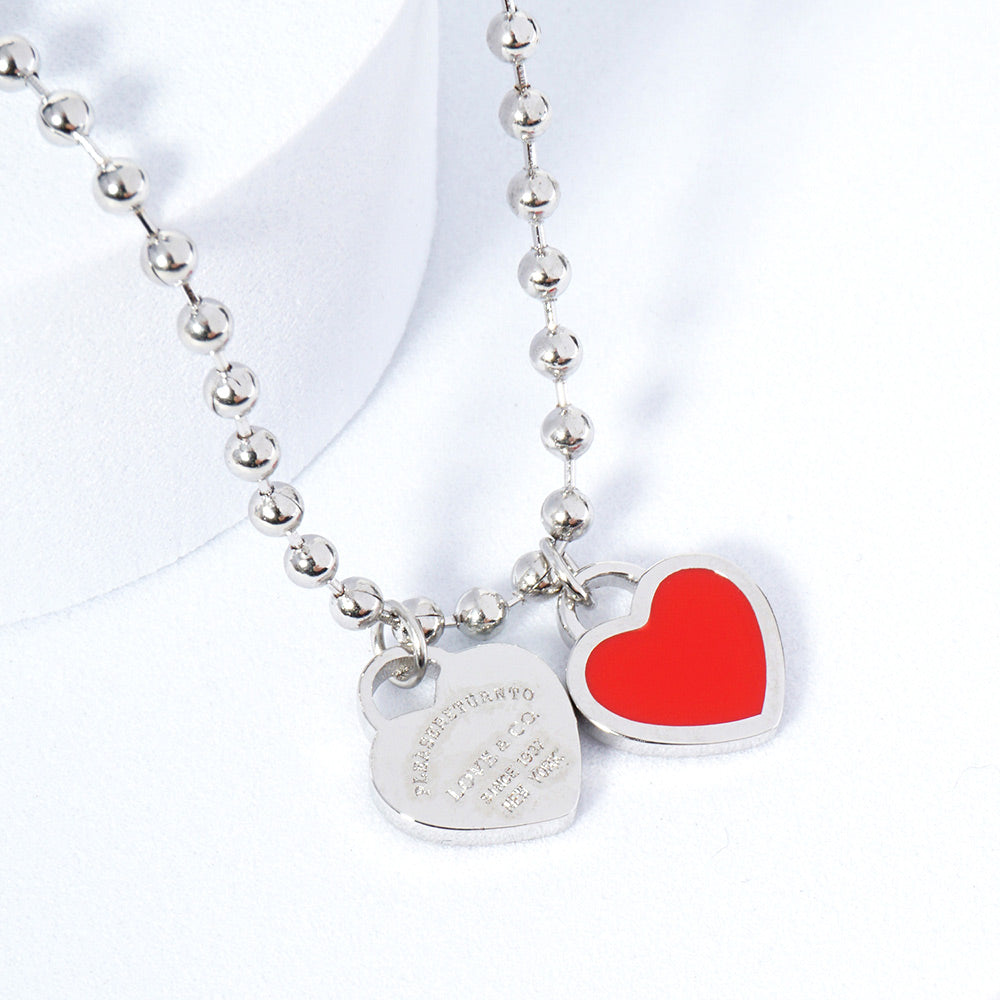A silver necklace featuring two heart-shaped charms on a ball chain.