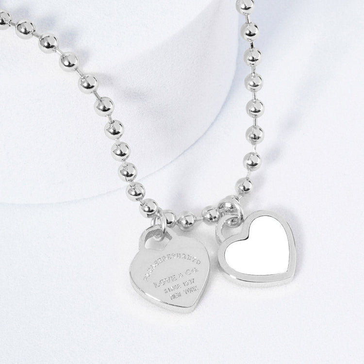 A silver necklace featuring two heart-shaped charms on a ball chain.